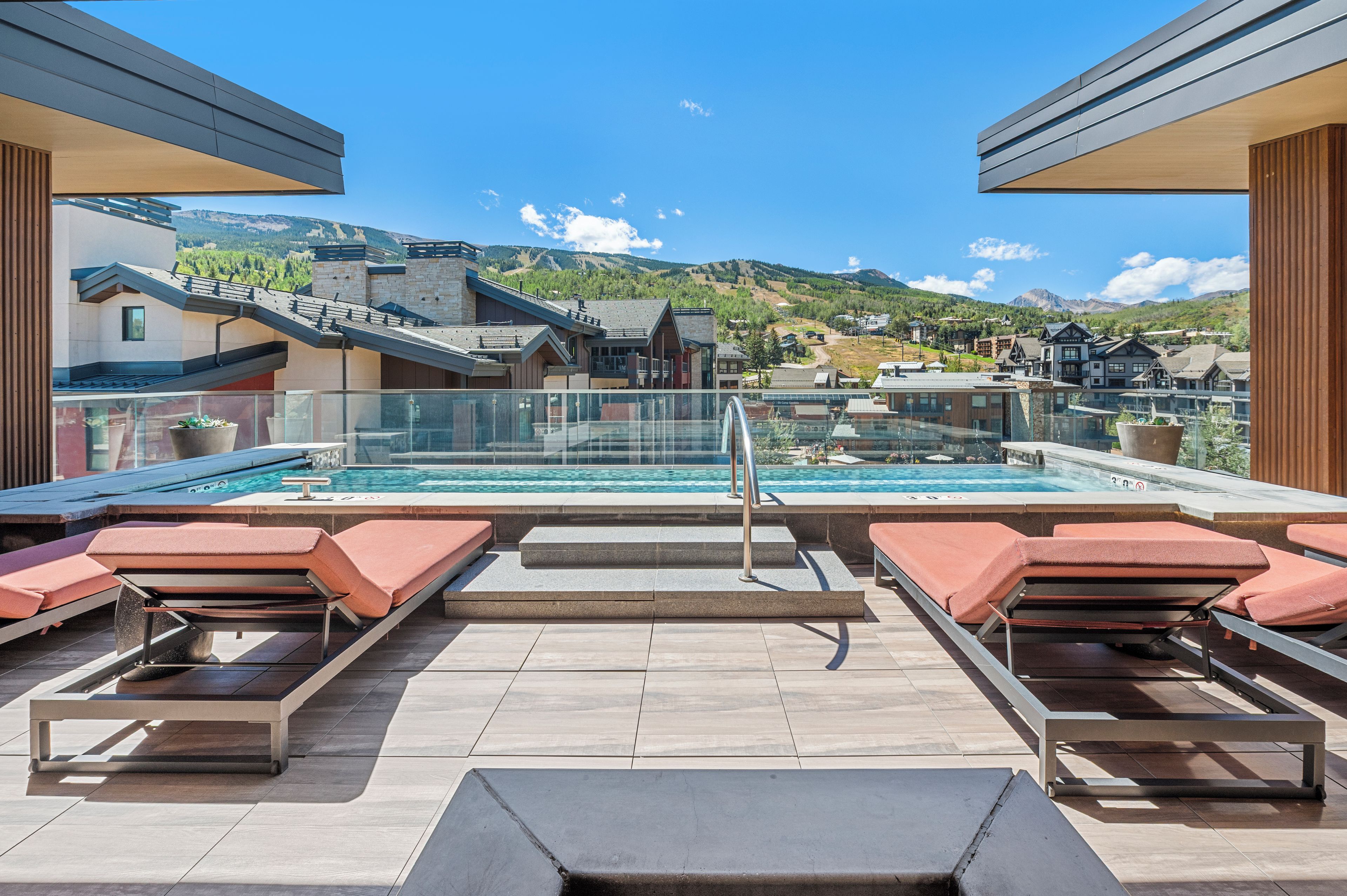 Un espace piscine aménagé sur le toit, avec des chaises longues et une vue sur une ville située dans un paysage montagneux.