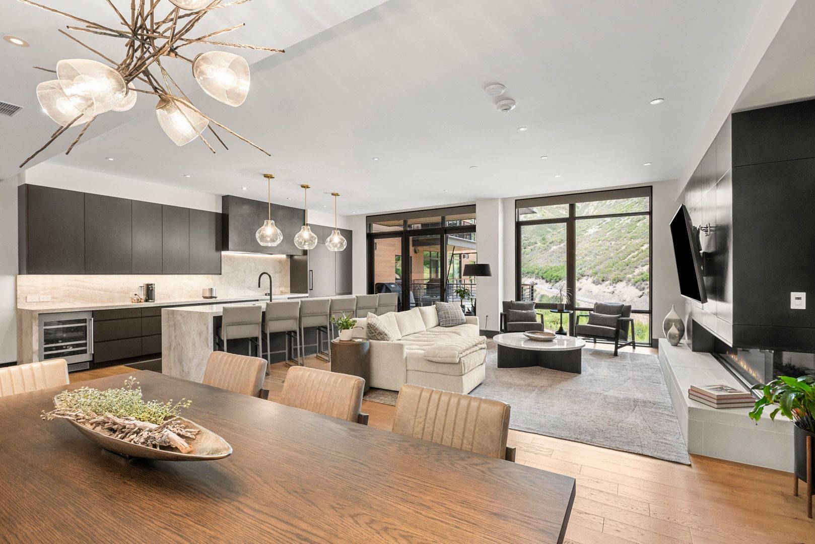 A modern kitchen with dark cabinetry, a dining area with a wooden table, and a living room with a sofa and a fireplace.