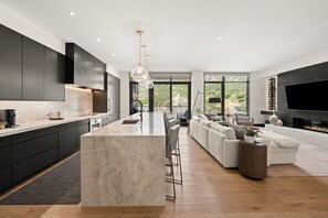 A modern kitchen with a large island, dark cabinetry, and a large TV in the living area. - Chateau Royale | One Snowmass East #605 | 4B/4B (Snowmass Village)