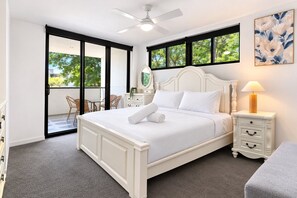 A bedroom with a bed, a nightstand, a lamp, a dresser, a mirror, and a view of the outdoors through large windows. - Elevated 3-Bed Apartment Close to Brisbane River (Saint Lucia)