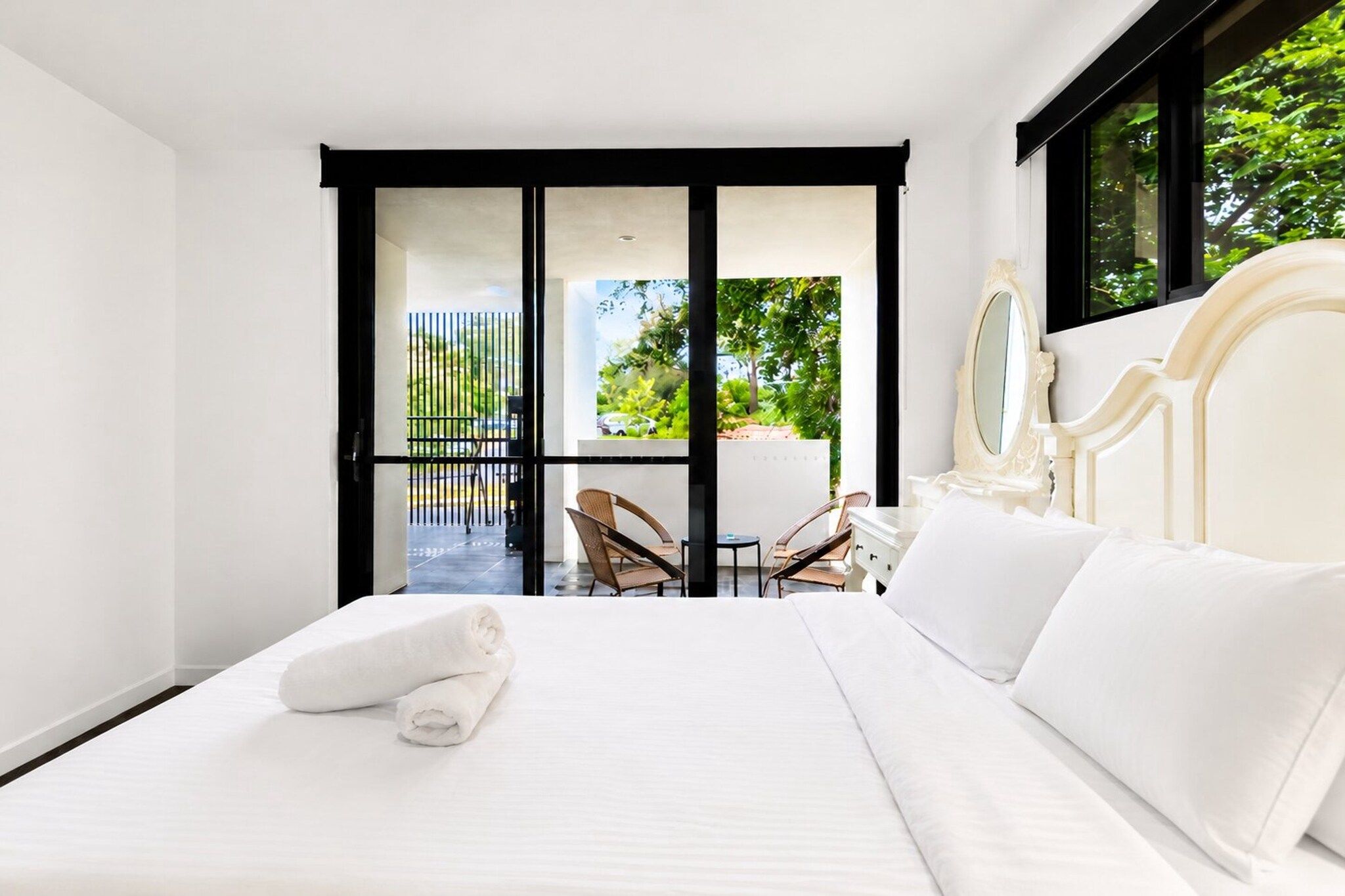 A hotel room with a bed, a chair, a table, and a balcony with a view of greenery.