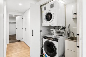 A laundry room with a front-loading washer and dryer, a basket, and a sink. - Elevated 3-Bed Apartment Close to Brisbane River (Saint Lucia)