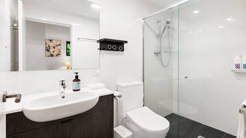 A modern bathroom with a white sink, dark wood vanity, a toilet, and a glass-enclosed shower.