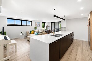 A modern kitchen with a large island, a dining area with a piano, and a living room with a sofa and a coffee table. - Elevated 3-Bed Apartment Close to Brisbane River (Saint Lucia)