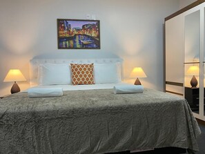 Quarto de hotel com cama, duas luminárias de cabeceira, um quadro na parede e um guarda-roupa.