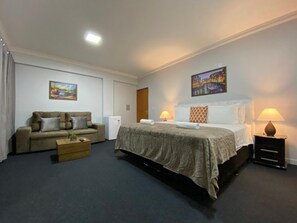 Quarto de hotel com cama, sofá, mesinha, luminária e um quadro na parede.