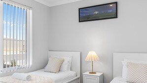 A bedroom with two beds, a nightstand with a lamp, and a window with blinds.