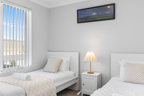 A bedroom with two beds, a nightstand with a lamp, and a window with blinds.