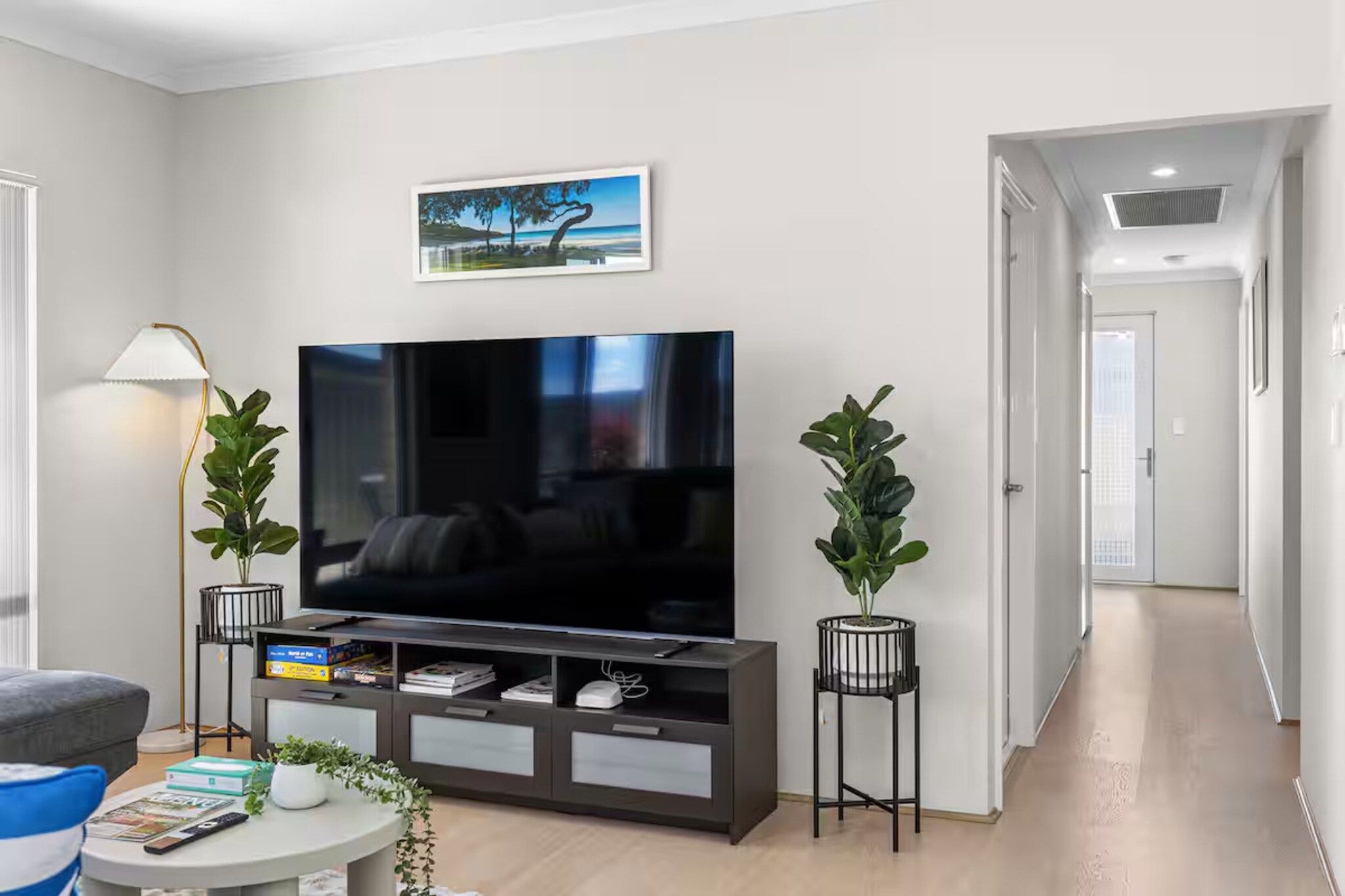 A modern living room with a flat-screen TV, a sofa, a coffee table, and two potted plants.