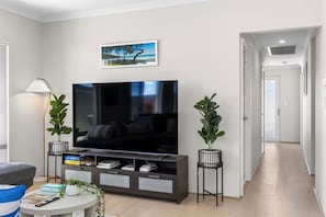 A modern living room with a flat-screen TV, a sofa, a coffee table, and two potted plants.