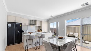 A modern kitchen with a central island, bar stools, and a dining table.