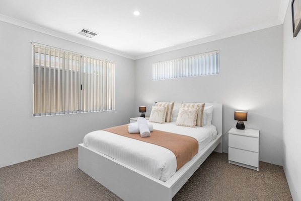 A modern bedroom with a large bed, two bedside tables, and a window with blinds.