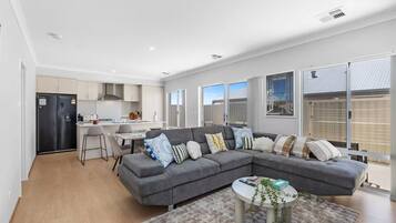 A modern living room with a grey sectional sofa, a small round coffee table, and a kitchen area with a fridge and cabinets.