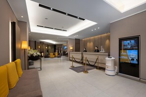 A modern hotel lobby with a reception desk, seating area, and a large digital screen displaying information. - Homeinn Select (Shenzhen)