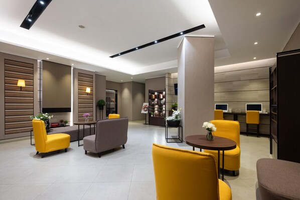 Eine moderne Hotelhalle mit Sitzbereichen, einer Rezeption und einem großen Bücherregal.
