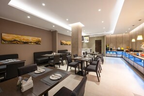 A modern dining area with tables and chairs, a kitchen in the background, and artwork on the walls. - Homeinn Select (Shenzhen)
