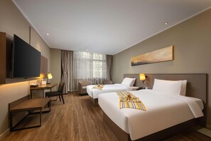 Ein Hotelzimmer mit zwei Betten, einem Schreibtisch, einem Stuhl, einem Fernseher und einem Fenster mit Vorhängen.