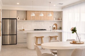 Una cocina moderna con una isla central, electrodomésticos de acero inoxidable, armarios de madera e iluminación colgante.