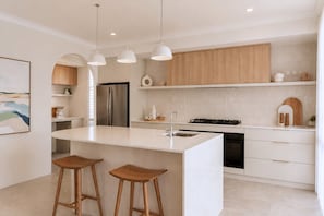 Een moderne keuken met een centraal eiland, houten barstoelen, een roestvrijstalen koelkast en een inbouwoven.