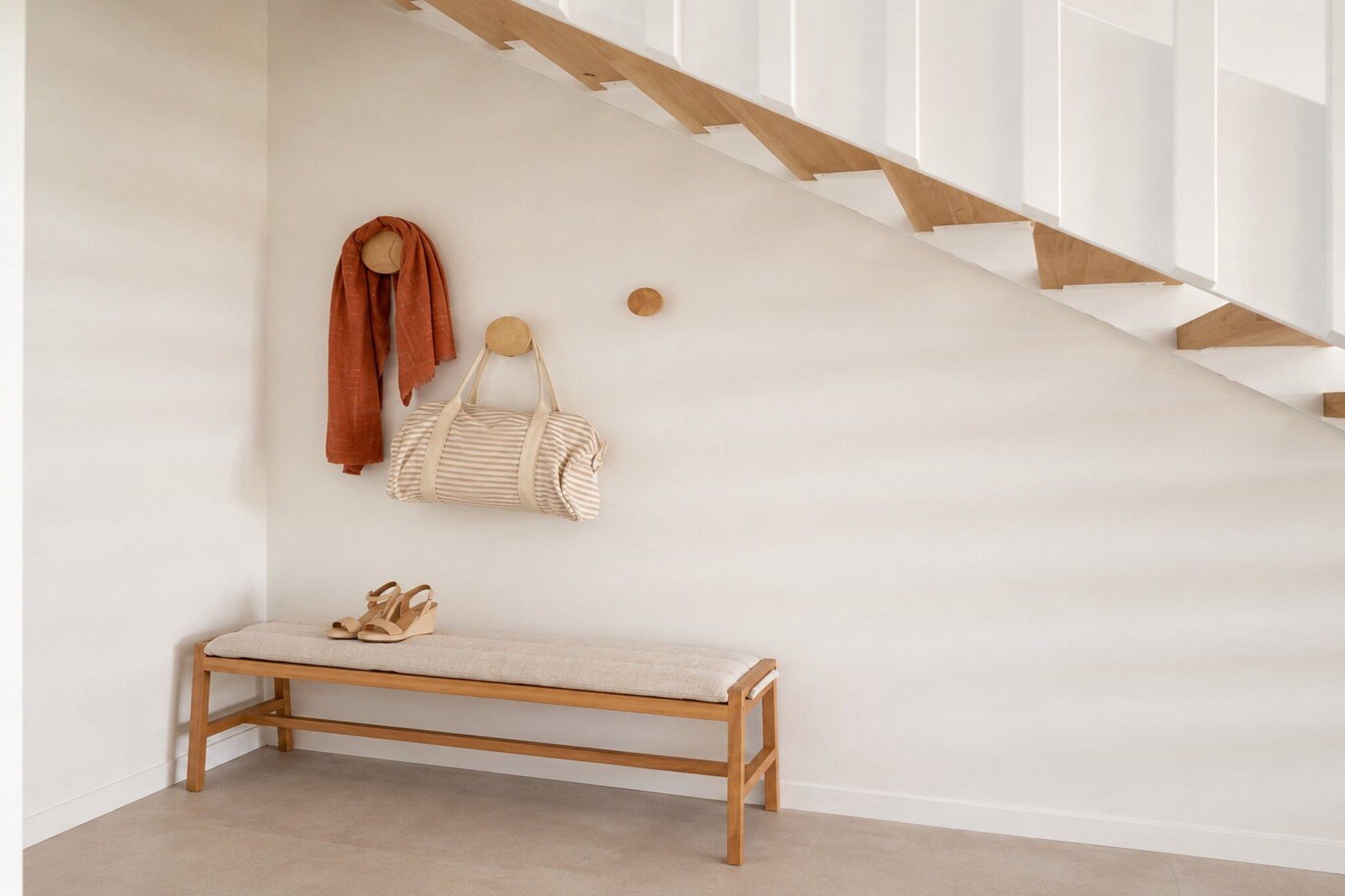A wooden bench with a cushion, a striped bag, and a scarf hanging on a wall.