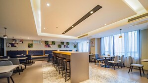 Un moderno vestíbulo de hotel con un bar central, zonas de estar y arte decorativo en la pared.