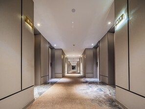 Passadís d'hotel amb sòl de moqueta, portes a ambdós costats i un llum al sostre.