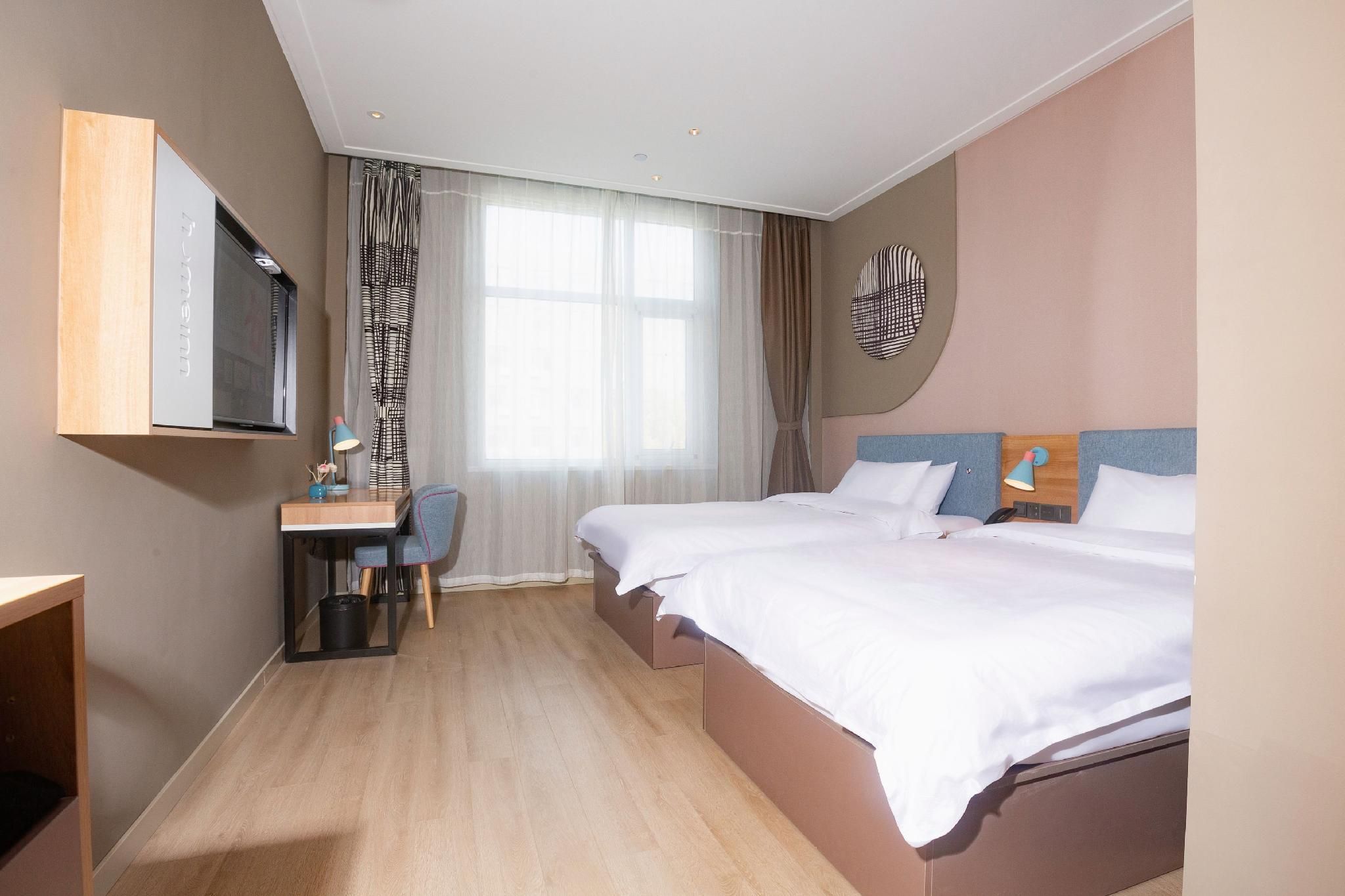 A hotel room with a bed, a desk, a chair, a television, and a window with curtains.