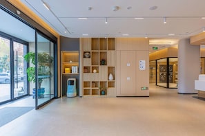 A modern reception area with a glass door entrance, a self-service kiosk, and a wooden shelving unit with various items.