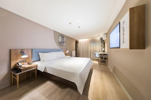 A hotel room with a bed, bedside table, lamp, and a desk with a chair.