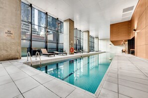 An indoor swimming pool with clear glass walls, lounge chairs, and a 'NO DIVING' sign indicating a depth limit. - High-Rise 1-Bed Apartment Near Southern Cross (Melbourne)