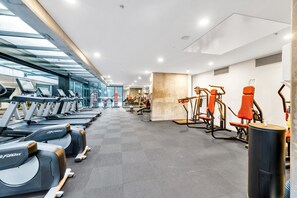 Ein Fitnessstudio mit Laufbändern, Kraftgeräten und einem an der Wand befestigten Hometrainer.