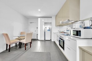 A modern kitchen with white cabinetry, a dining area with a glass table and cushioned chairs, and a microwave oven. - High-Rise 1-Bed Apartment Near Southern Cross (Melbourne)