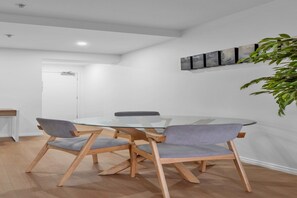 A modern dining area with a round glass table and four chairs with wooden frames and grey cushions. - Bright 1-Bed Apartment Near Royal Botanic Gardens (Southbank)