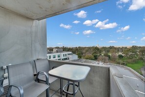 Varanda com mesa e cadeiras, vista para a paisagem urbana com edifícios e árvores.