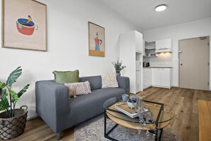A modern living room with a grey sofa, a glass coffee table, and a kitchen with white cabinets. - Stylish 2-Bed Apartment Near Melbourne Central (Carlton)