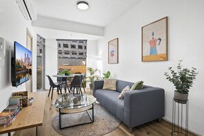 A modern living room with a grey sofa, a glass coffee table, and a TV on the wall. - Stylish 2-Bed Apartment Near Melbourne Central (Carlton)