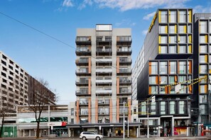 A modern multi-story building with balconies, a parking area, and a storefront. - Stylish 2-Bed Apartment Near Melbourne Central (Carlton)