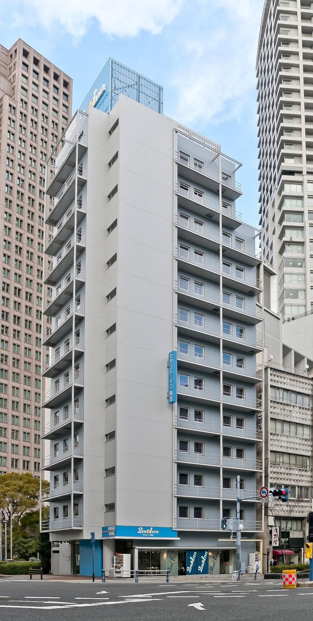 Ein mehrstöckiges Hotel mit moderner Fassade, das an einer Straßenecke zwischen anderen Gebäuden liegt.