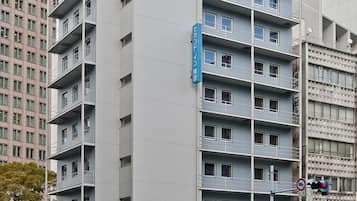 A multi-story hotel with a modern facade, located at a street corner with other buildings.