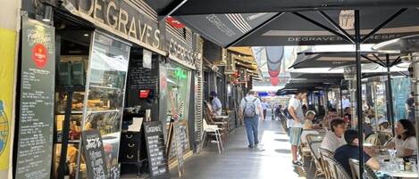 Um café ao ar livre com mesas e cadeiras, um letreiro com 'DEGRAVES' espresso e um quadro de menu.
