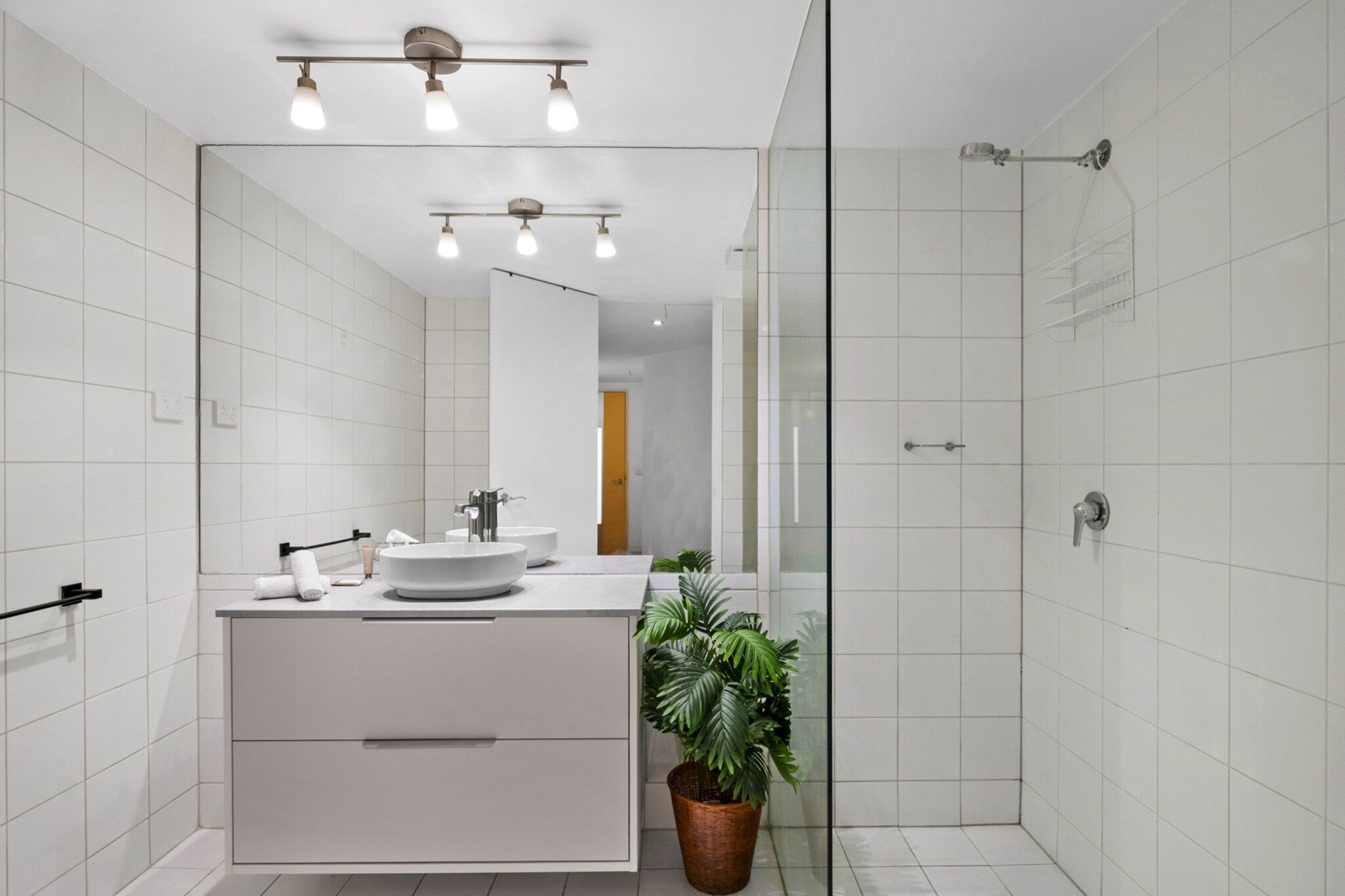 Ein modernes Badezimmer mit großem Spiegel, einem runden Waschbecken, einer Dusche und einer Topfpflanze.