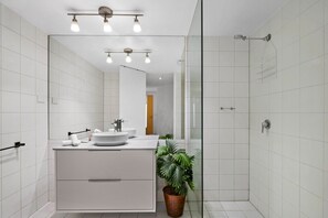 Et moderne badeværelse med et stort spejl, en rund vask, en bruser og en potteplante.