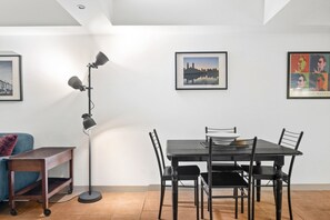 A dining area with a table and chairs, a floor lamp, and two framed pictures on the wall. - Melbourne 1-Bed Apartment Flinders Street (Melbourne)