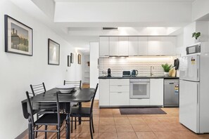 Een moderne keuken met witte kasten, een zwart aanrecht en een eethoek met een tafel en stoelen.