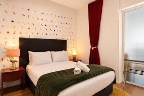 A hotel room with a bed, a nightstand, a lamp, a red curtain, and a window with a metal rack. - Empire Theatre Loft |Your Colourful Melbourne Stay (Melbourne)