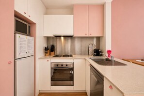 Une cuisine compacte avec des meubles blancs, un four en acier inoxydable, un lave-vaisselle et un évier.