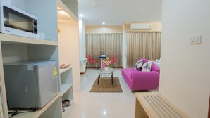 A modern living room with a sofa, a coffee table, and a dining area with chairs. - Taragrand Donmuang Airport Hotel (Thanyaburi)