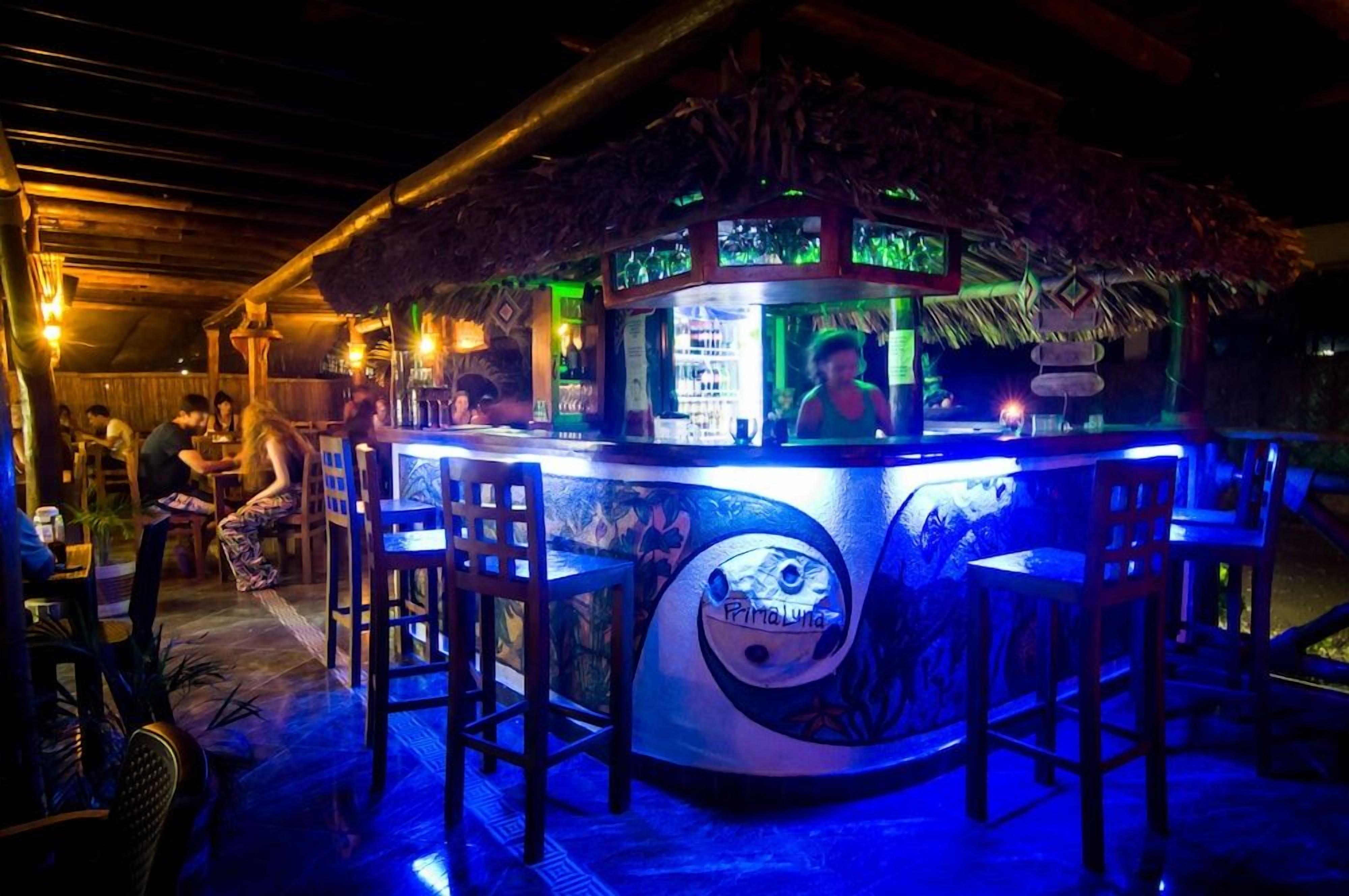 Un bar tiki con techo de paja, taburetes y una barra con un letrero de neón.