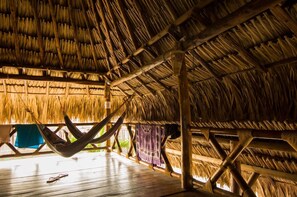 A thatched-roof room with a hammock, wooden floor, and a view of the outdoors. - Primaluna Beach Hostel (Dibulla)
