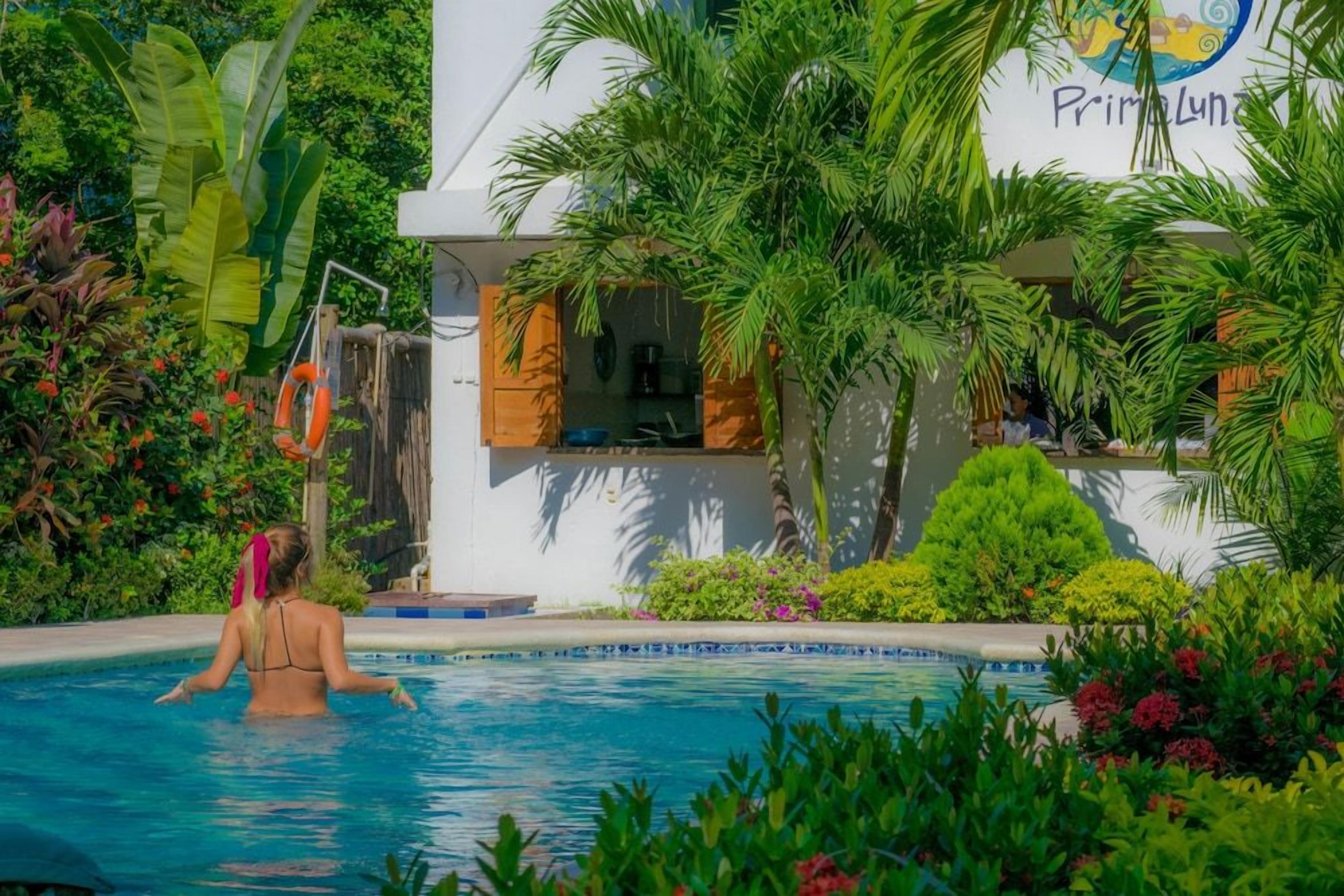 Una piscina rodeada de exuberante vegetación y un edificio con un cartel que dice 'Primeluna'.
